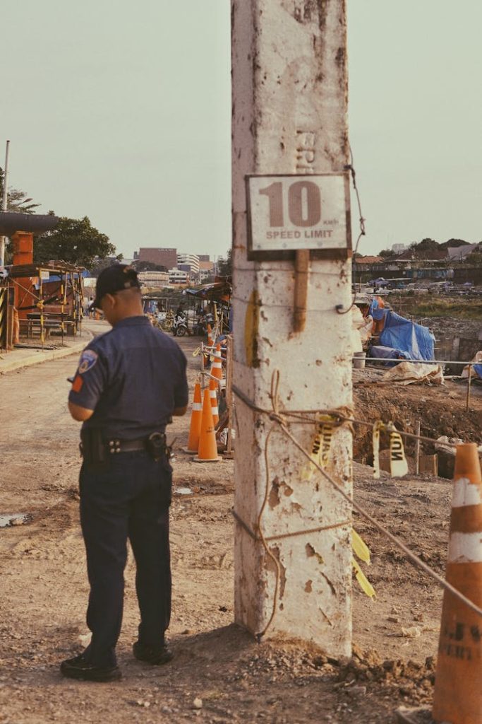 Police officer standing at a construction site near a speed limit sign, ensuring safety.